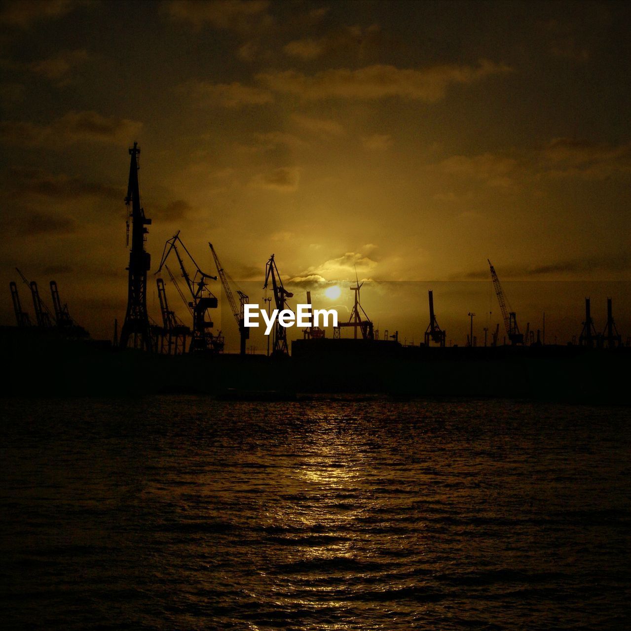 Silhouette cranes at commercial dock against sky during sunset