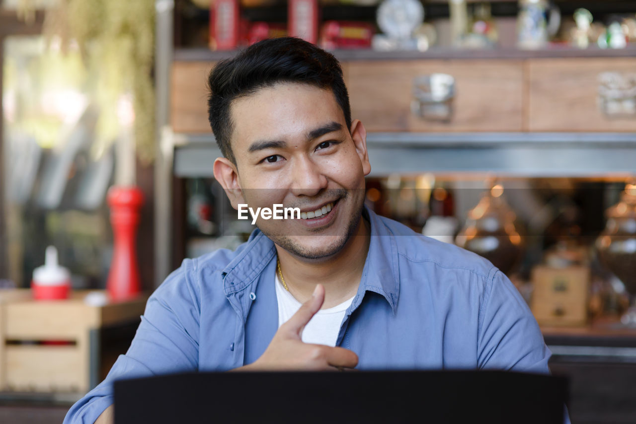 Portrait of smiling male owner showing thumbs up sign at cafe