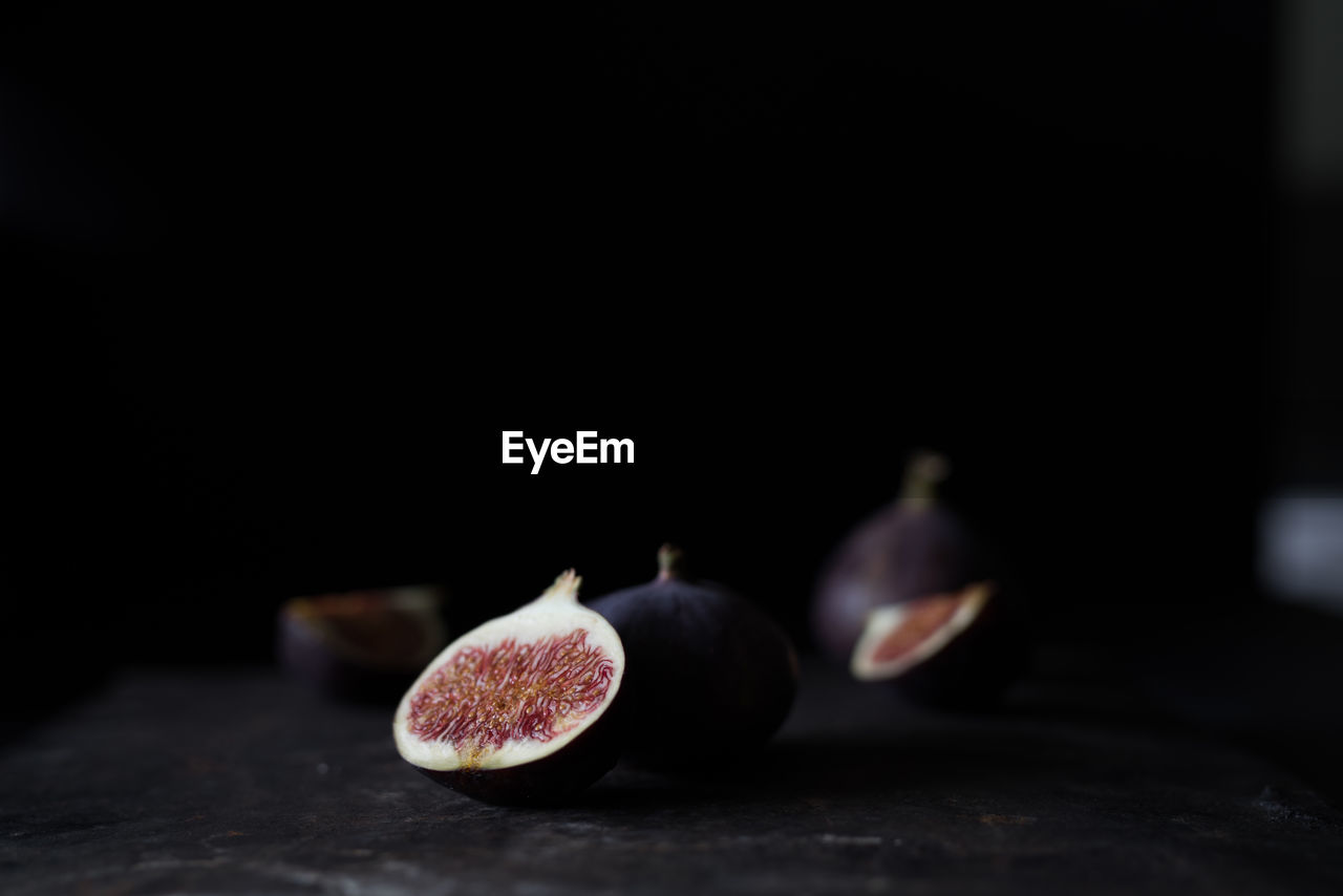 Halved and whole figs against black background