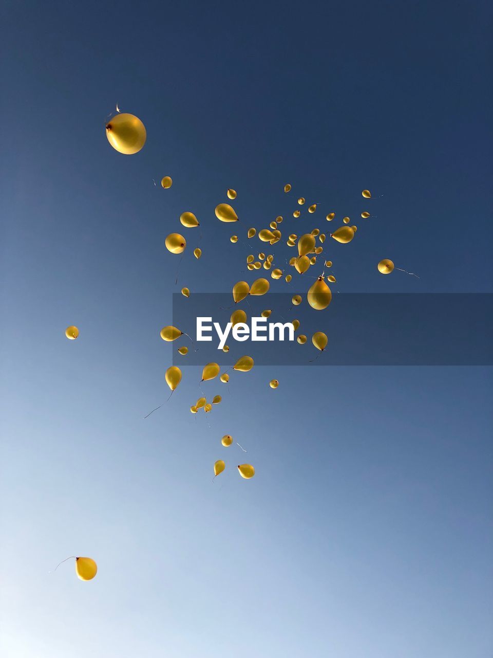 Low angle view of yellow balloons flying against blue sky