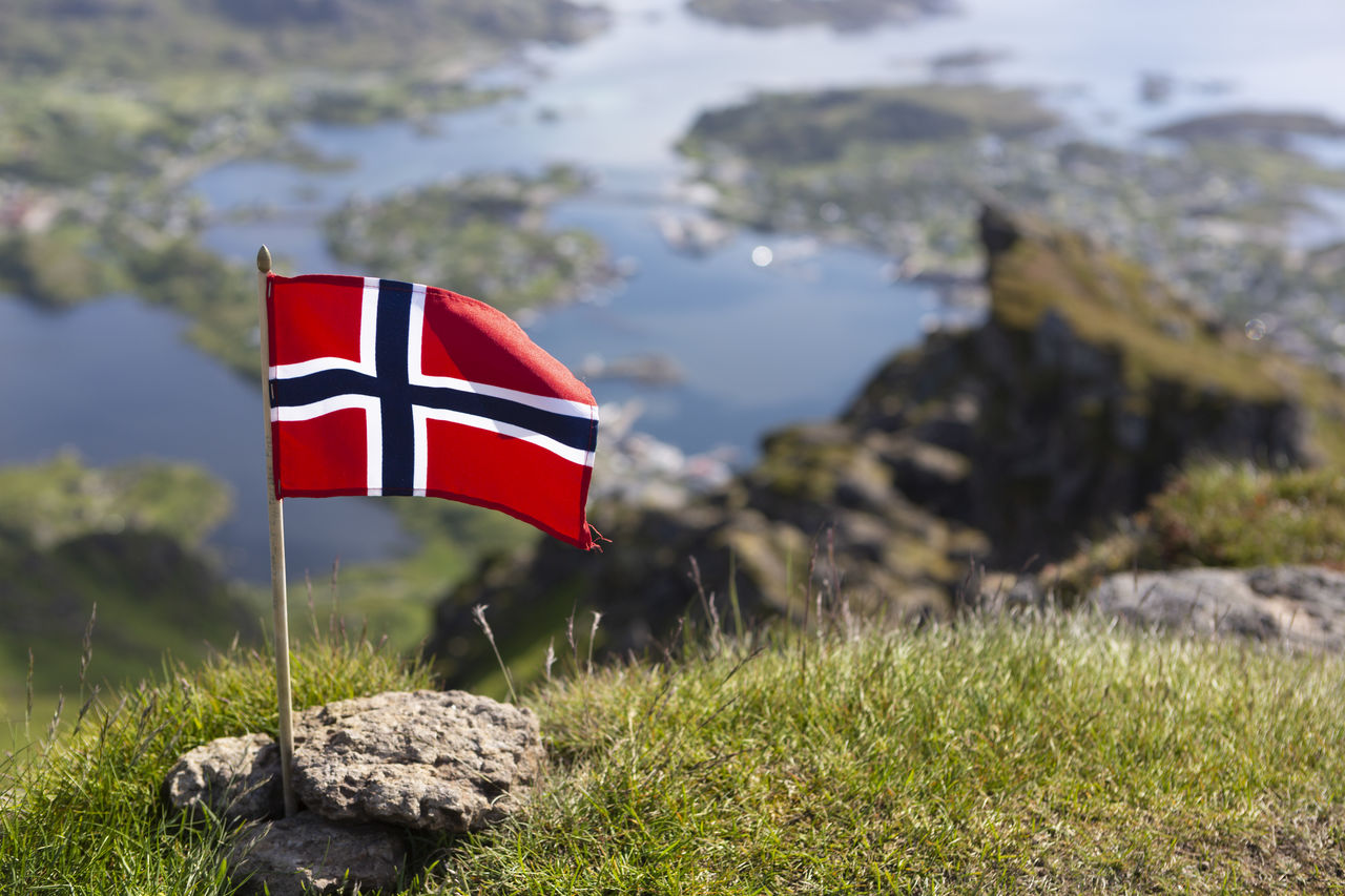 Norwegian flag on the nonstinden mountain. in the background ballstad, lofoten islands, norway