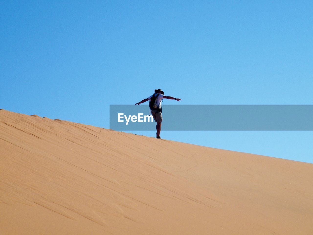 Low angle view of man standing on desert against clear blue sky