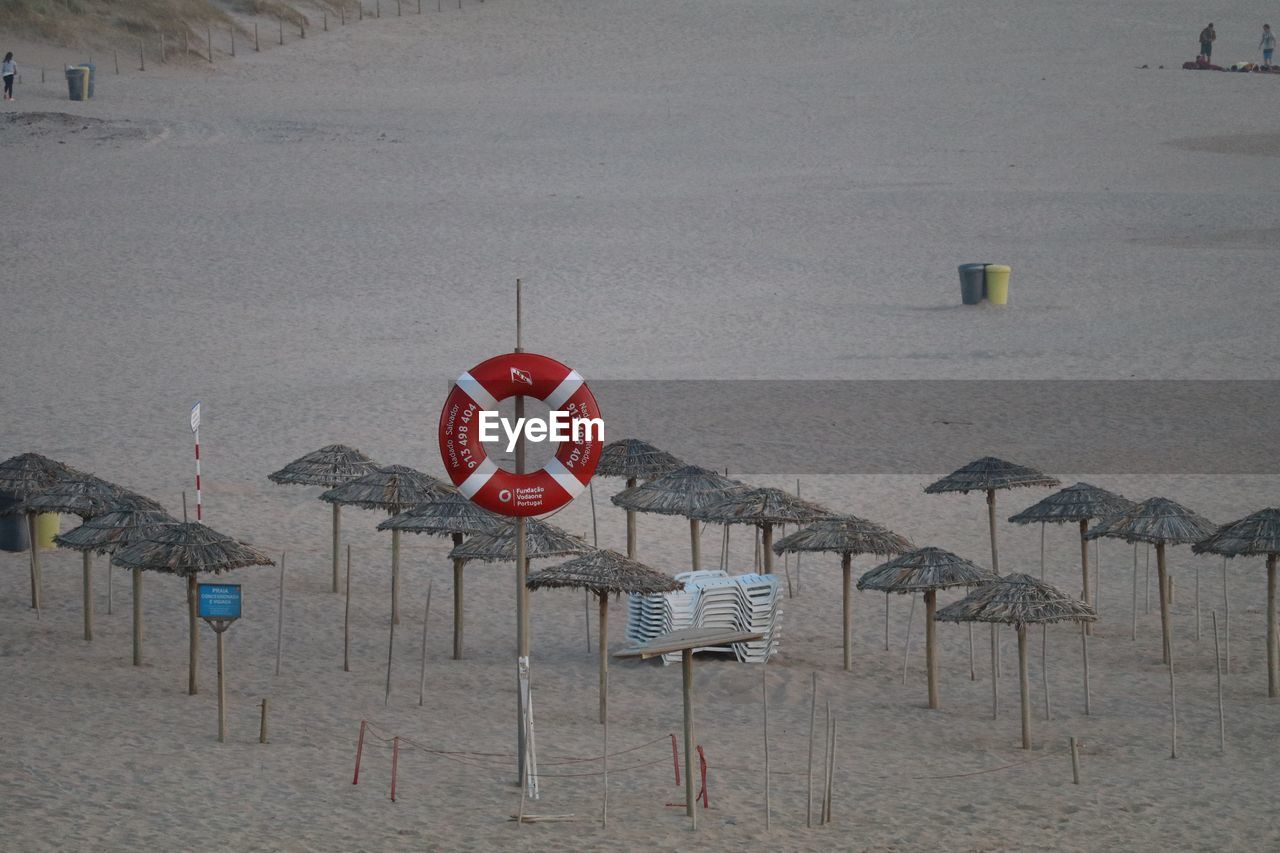 High angle view of life belt hanging on pole by straw parasols at beach