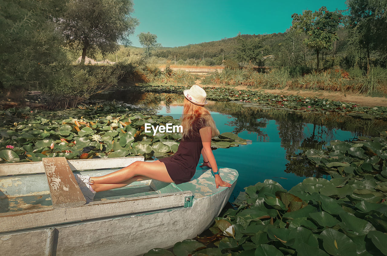 Carefree young woman floating relaxed on a boat at a pond with blooming waterlily, lotus flowers.