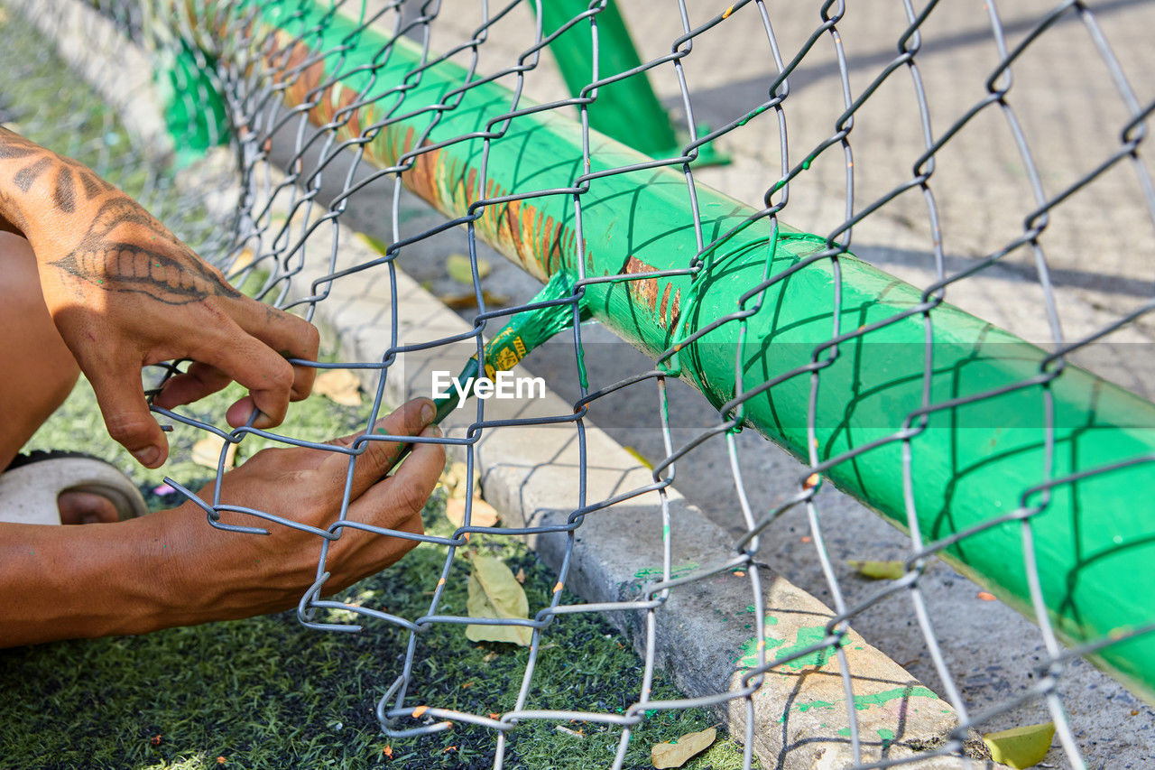 one person, hand, fence, day, nature, men, outdoors, lifestyles, leisure activity, adult, metal, net, high angle view, chainlink fence, sports, close-up
