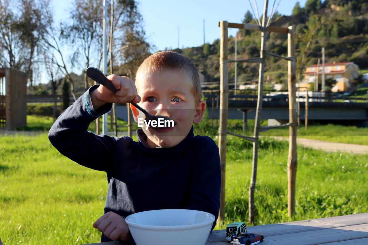 A blond boy with a big spoon in his mouth and surprised eyes. a boy is perplexed by what he sees.