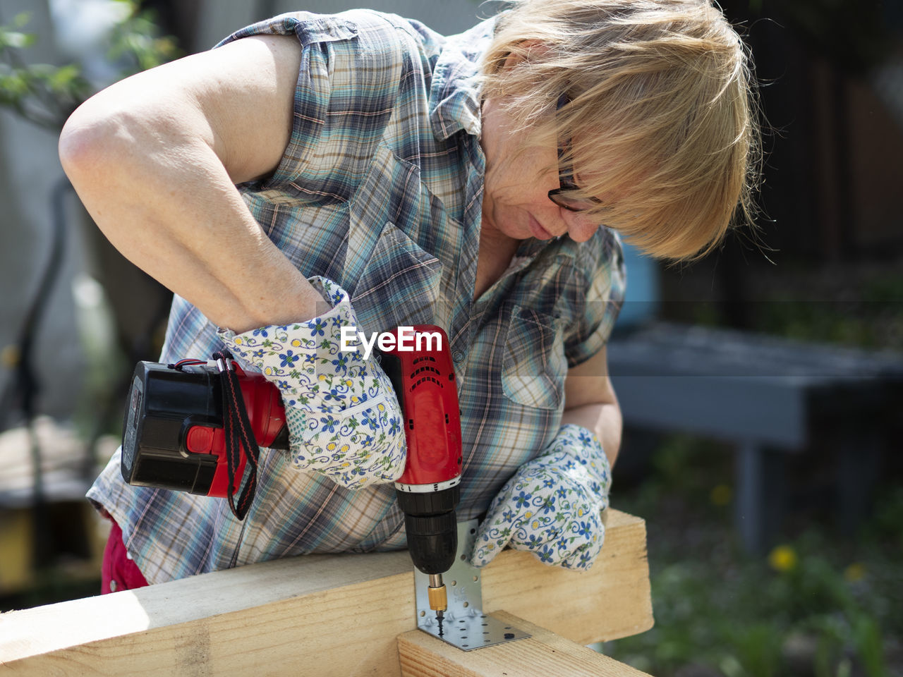 Senior caucasian woman assembles a wooden frame of building using metal fasteners using screwdriver