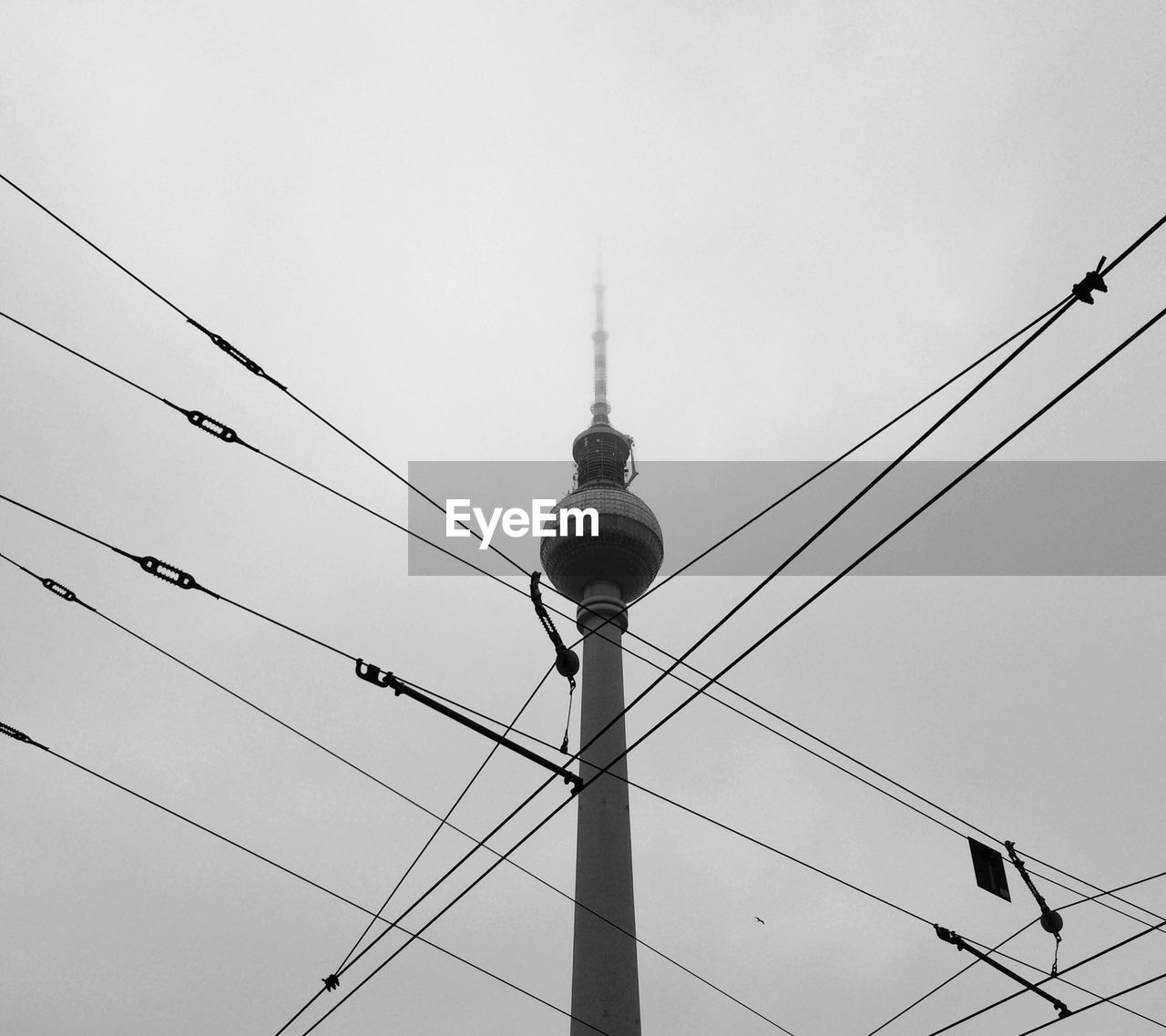 Low angle view of fernsehturm and cables during foggy weather