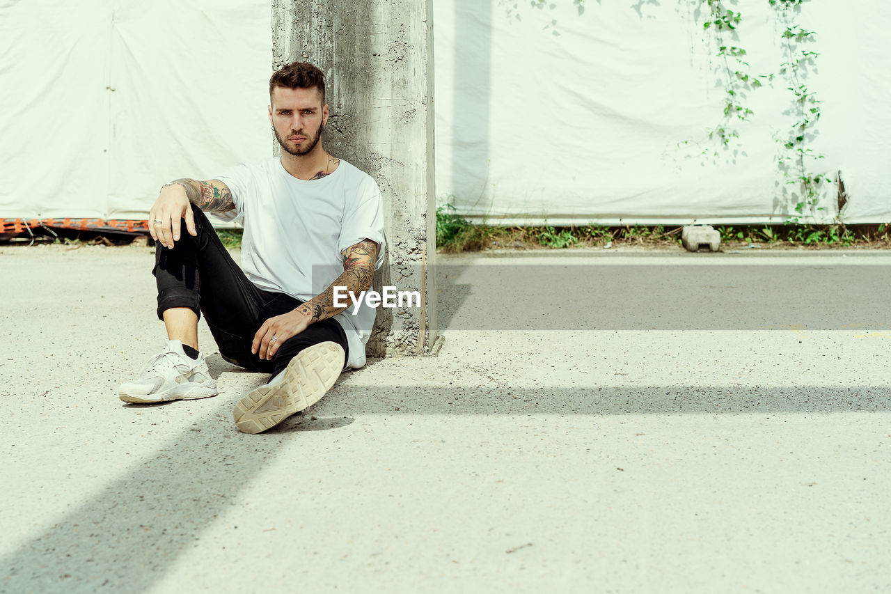 Portrait of handsome young man sitting on footpath