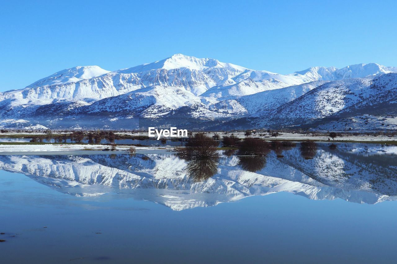 SCENIC VIEW OF SNOWCAPPED MOUNTAINS BY LAKE AGAINST BLUE SKY