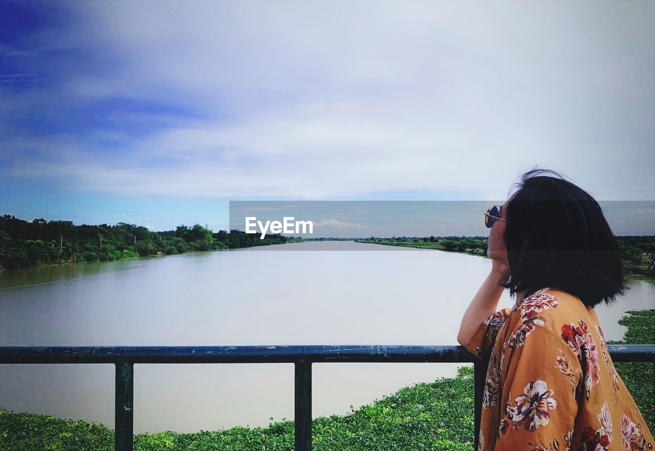 Side view of woman looking at lake while standing by railing