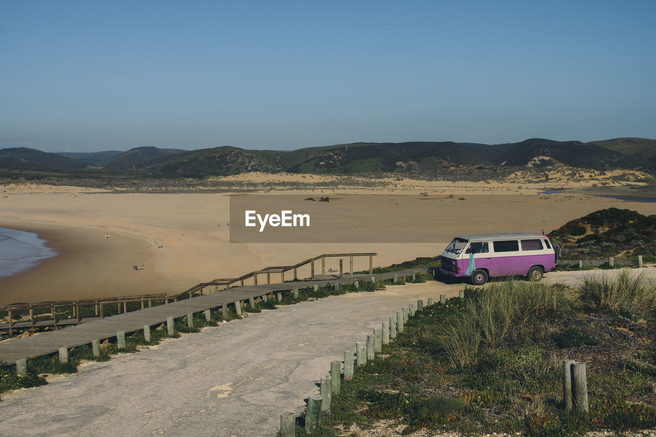 Van on road by beach against clear sky