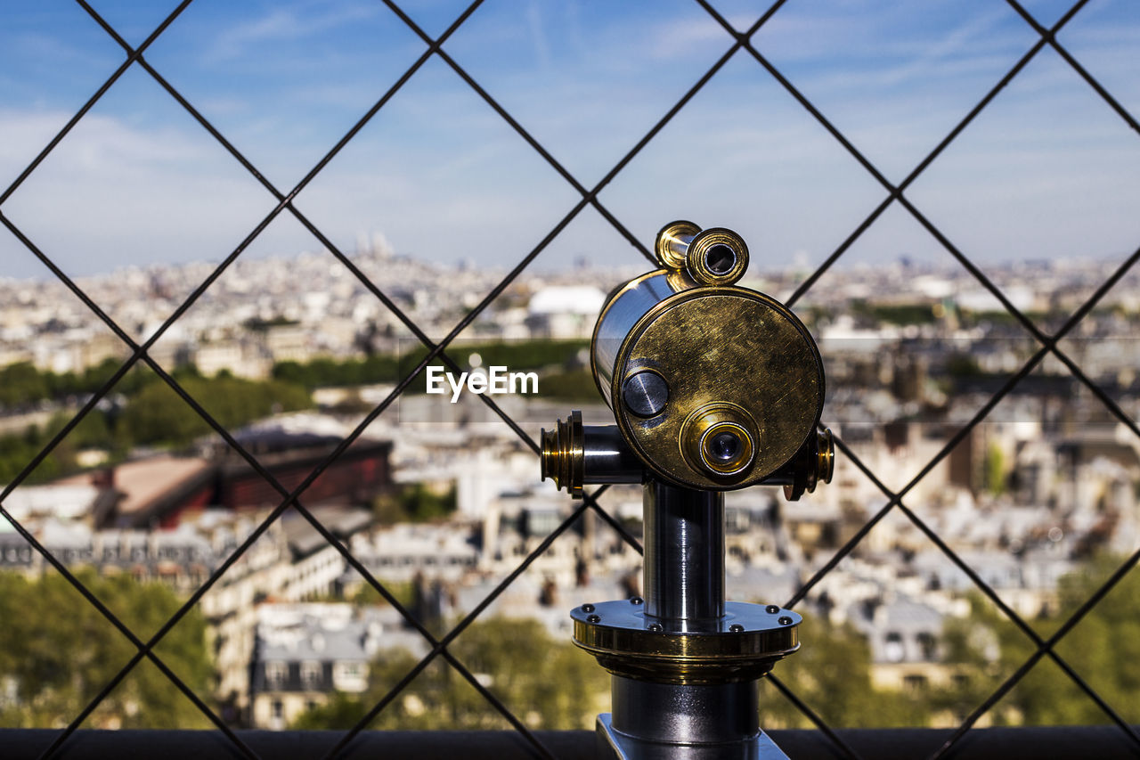 CLOSE-UP OF COIN-OPERATED BINOCULARS BY CITYSCAPE AGAINST SKY