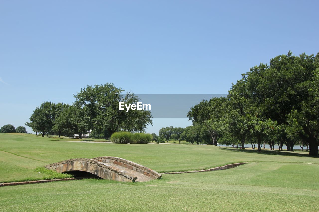 Footbridge at golf course against clear sky