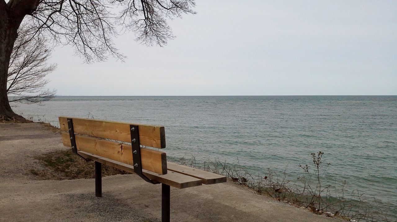 Empty bench by sea against sky