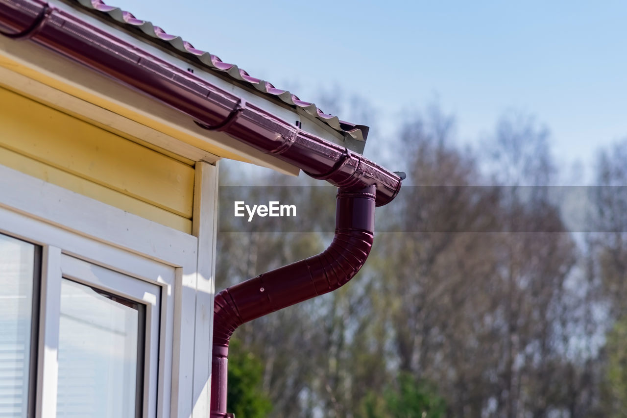 Corner of the house with gutter on a background of blue sky and spring forest