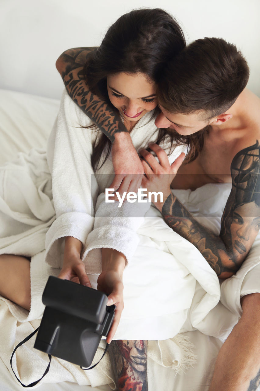 High angle view of couple holding camera sitting on bed