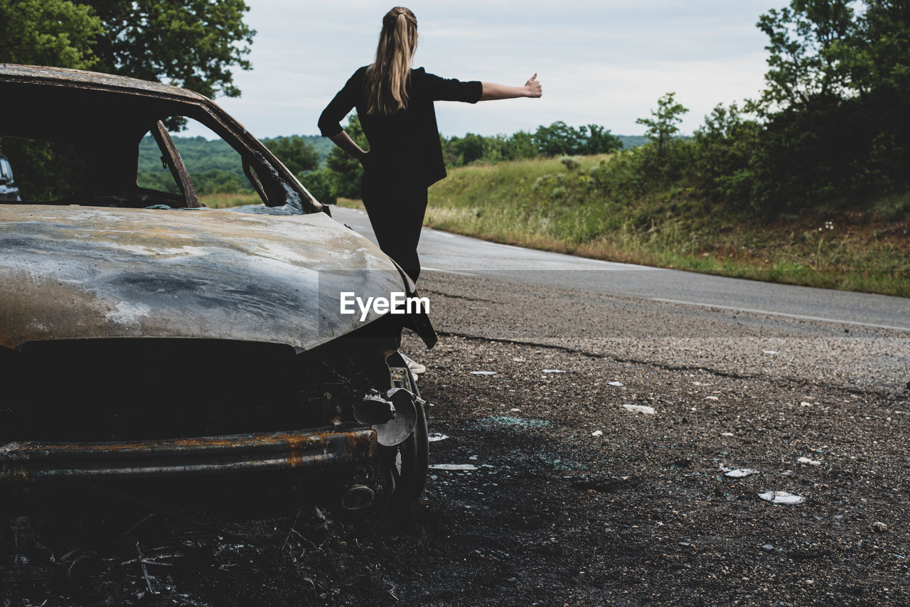 LOW SECTION OF WOMAN STANDING ON ROAD AGAINST TREES