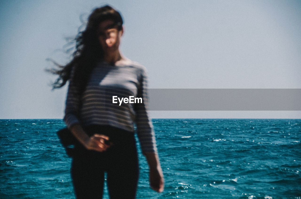 Woman with tousled hair standing at beach against clear sky