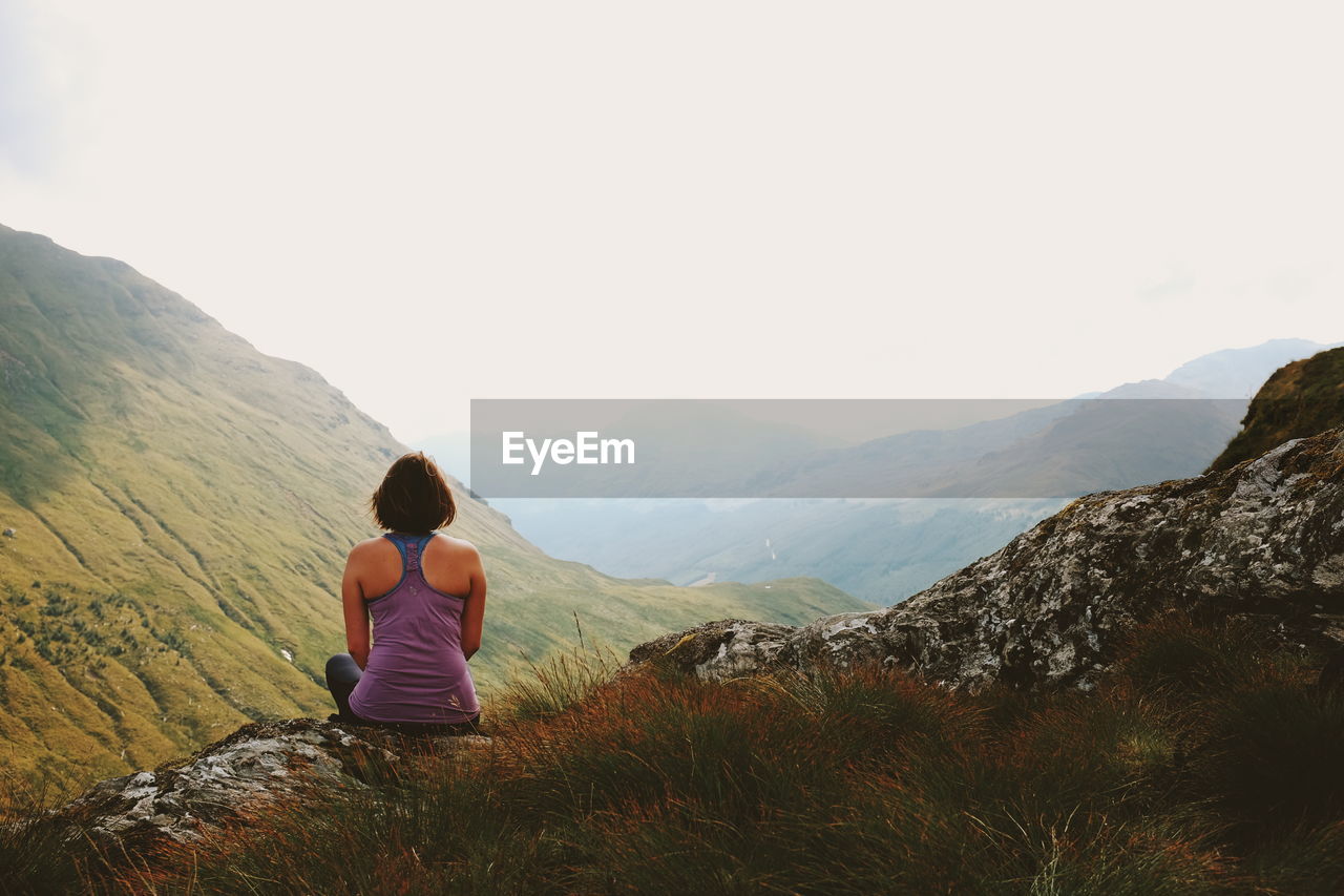 Rear view of woman sitting on mountain against sky