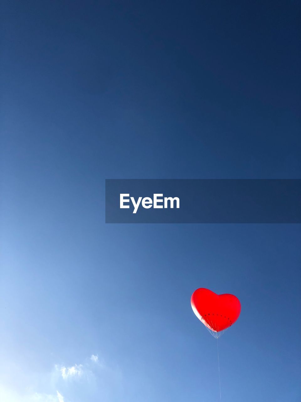 Low angle view of red heart shaped balloon flying against blue sky