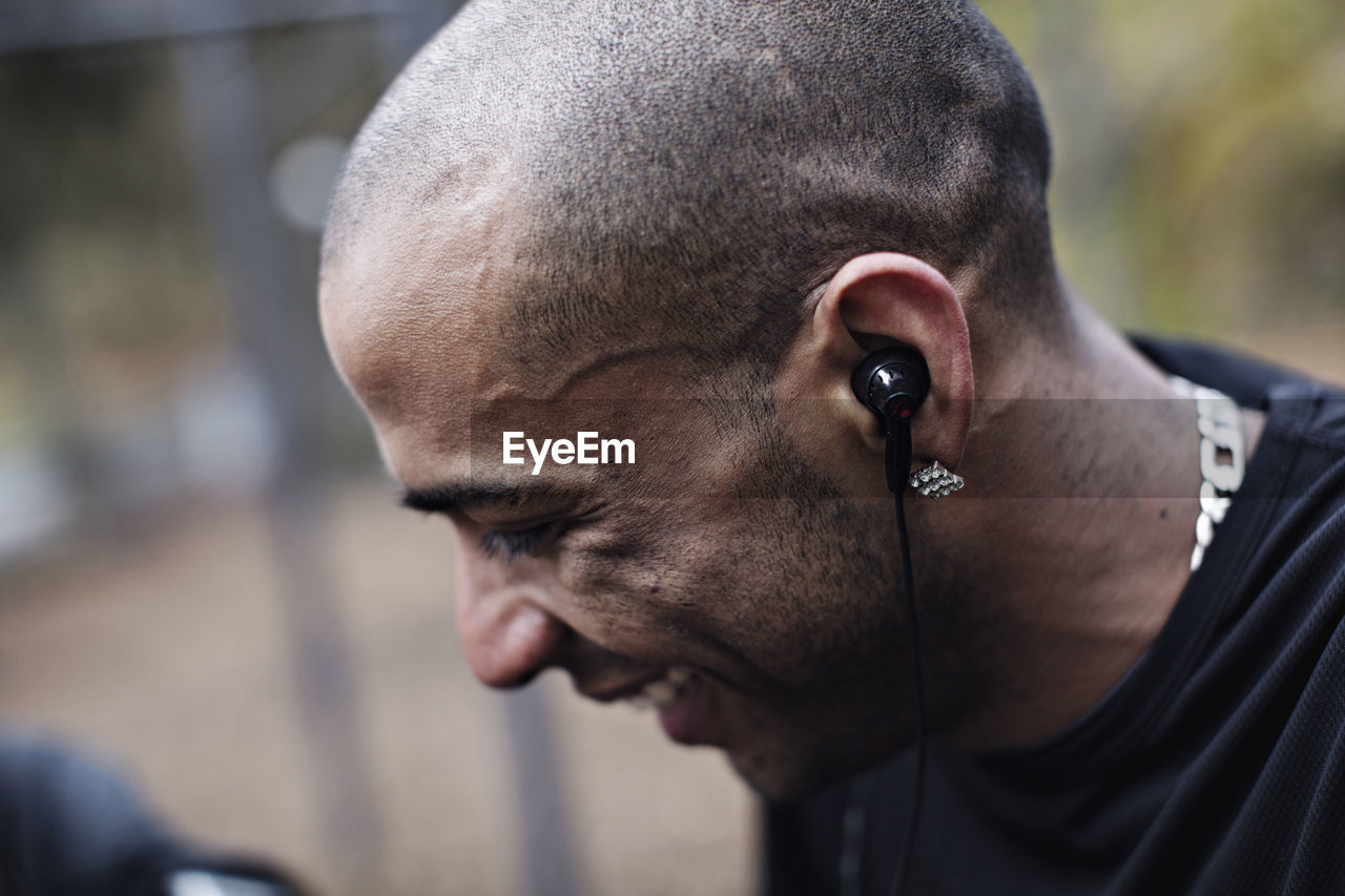 Side view of happy male athlete wearing in-ear headphones at forest