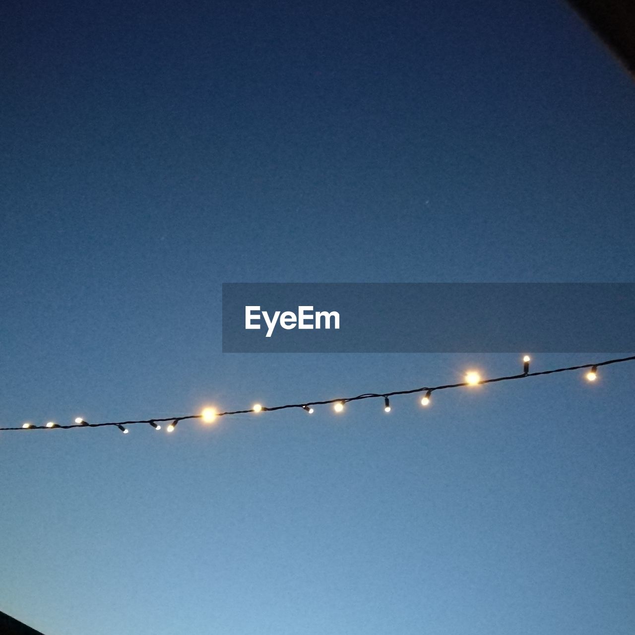 LOW ANGLE VIEW OF ILLUMINATED LIGHTS AGAINST CLEAR BLUE SKY