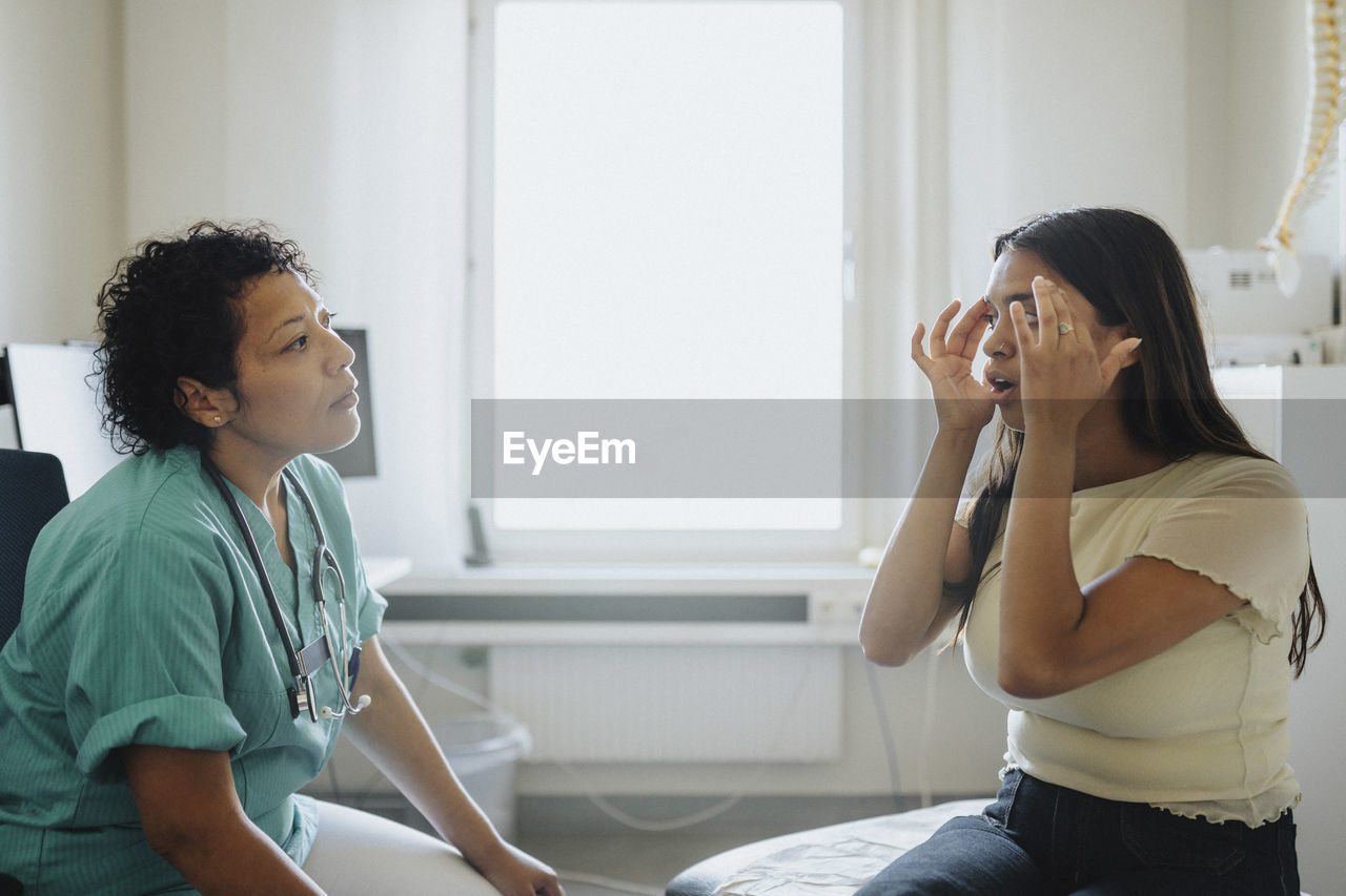 Young woman touching head while discussing with female physician in clinic