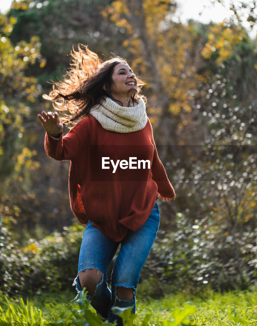 Woman in red sweater dancing happily on a meadow in a forest.