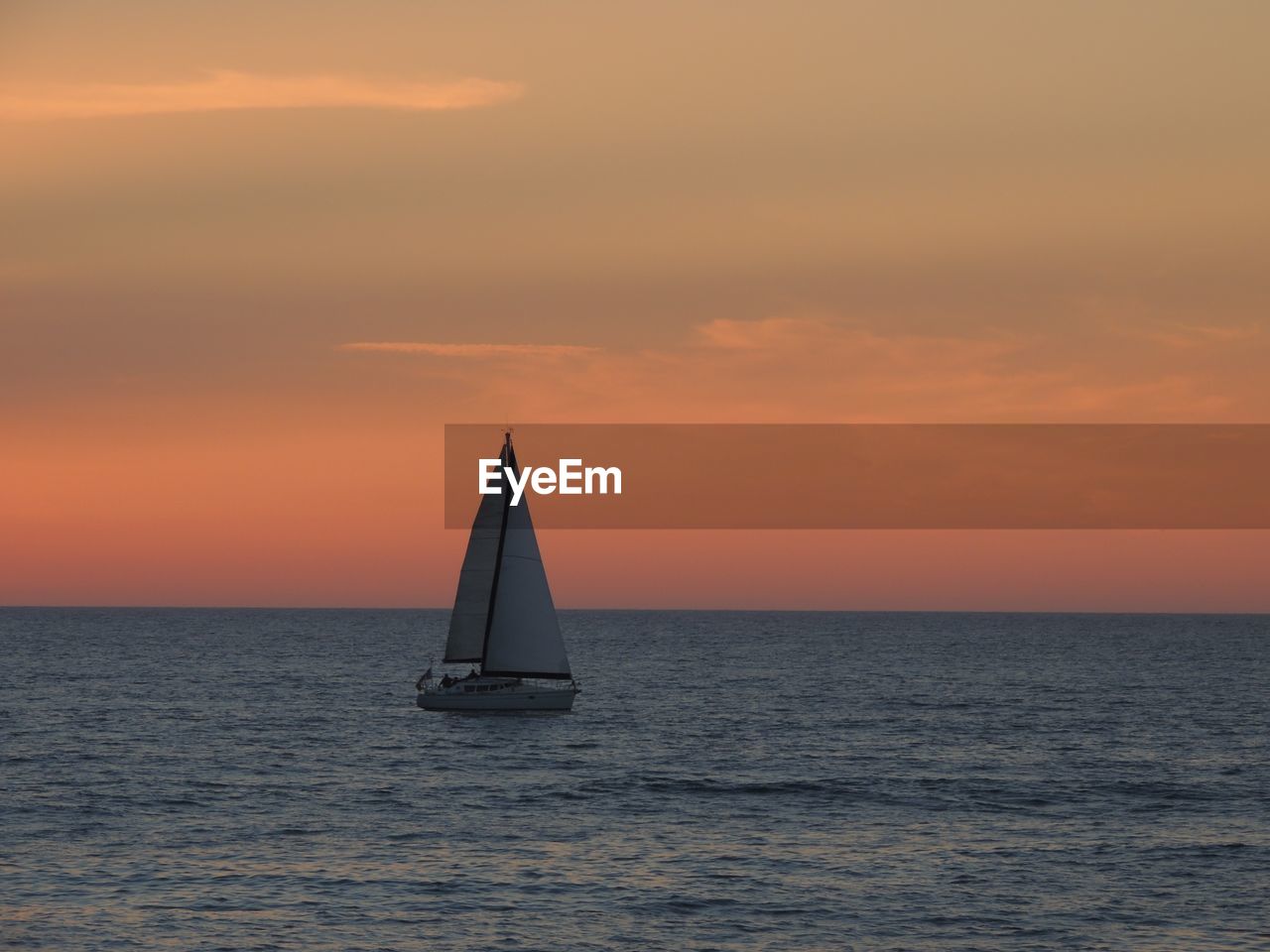 Sailboat sailing on sea against orange sky