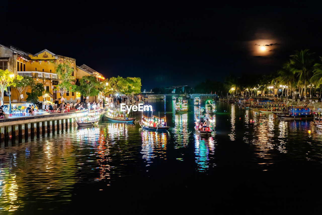 ILLUMINATED BUILDINGS BY RIVER AGAINST SKY