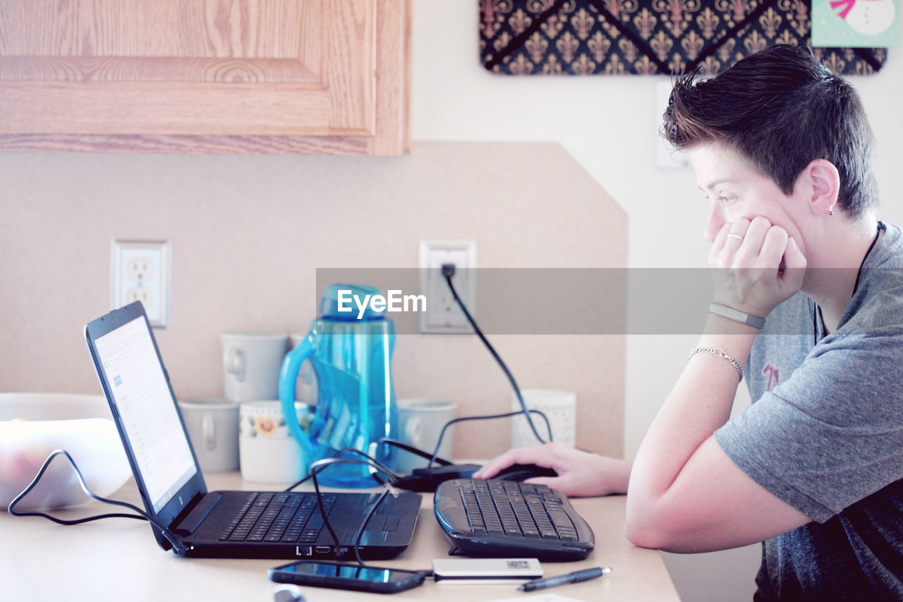 Side view of woman using laptop at home