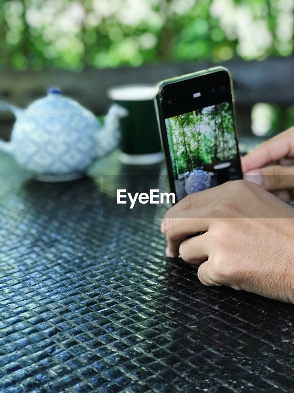 Cropped hands of man photographing with mobile phone at table in cafe