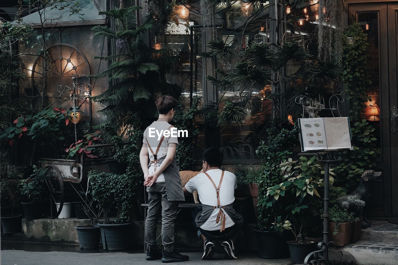 REAR VIEW OF MAN STANDING AT ILLUMINATED SHOP