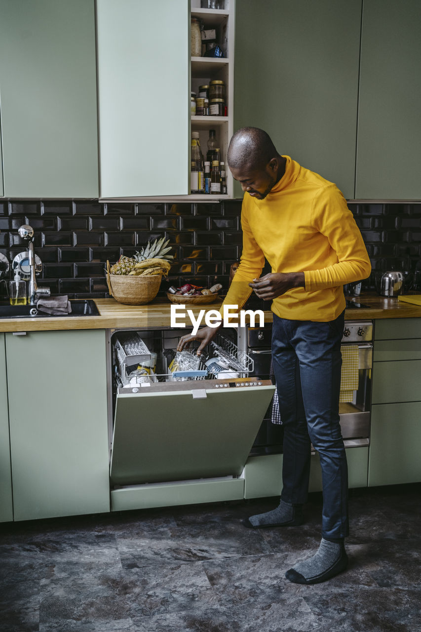 Full length of mid adult man doing dishes in kitchen at home