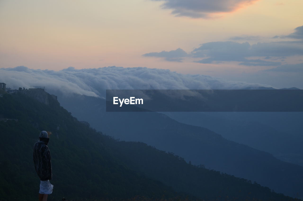 Rear view of man standing on mountain against sky