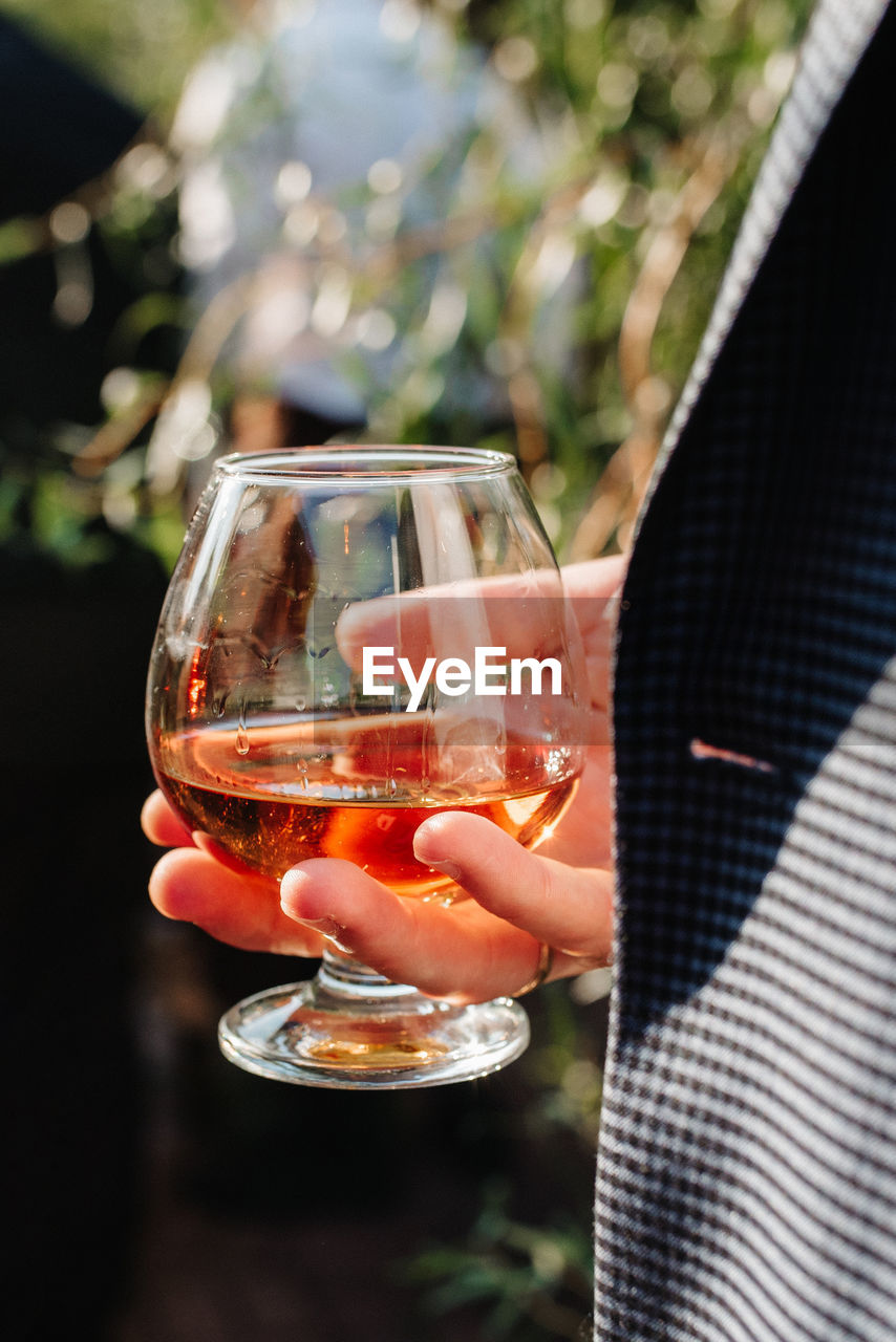 MIDSECTION OF WOMAN HOLDING GLASS OF WINE