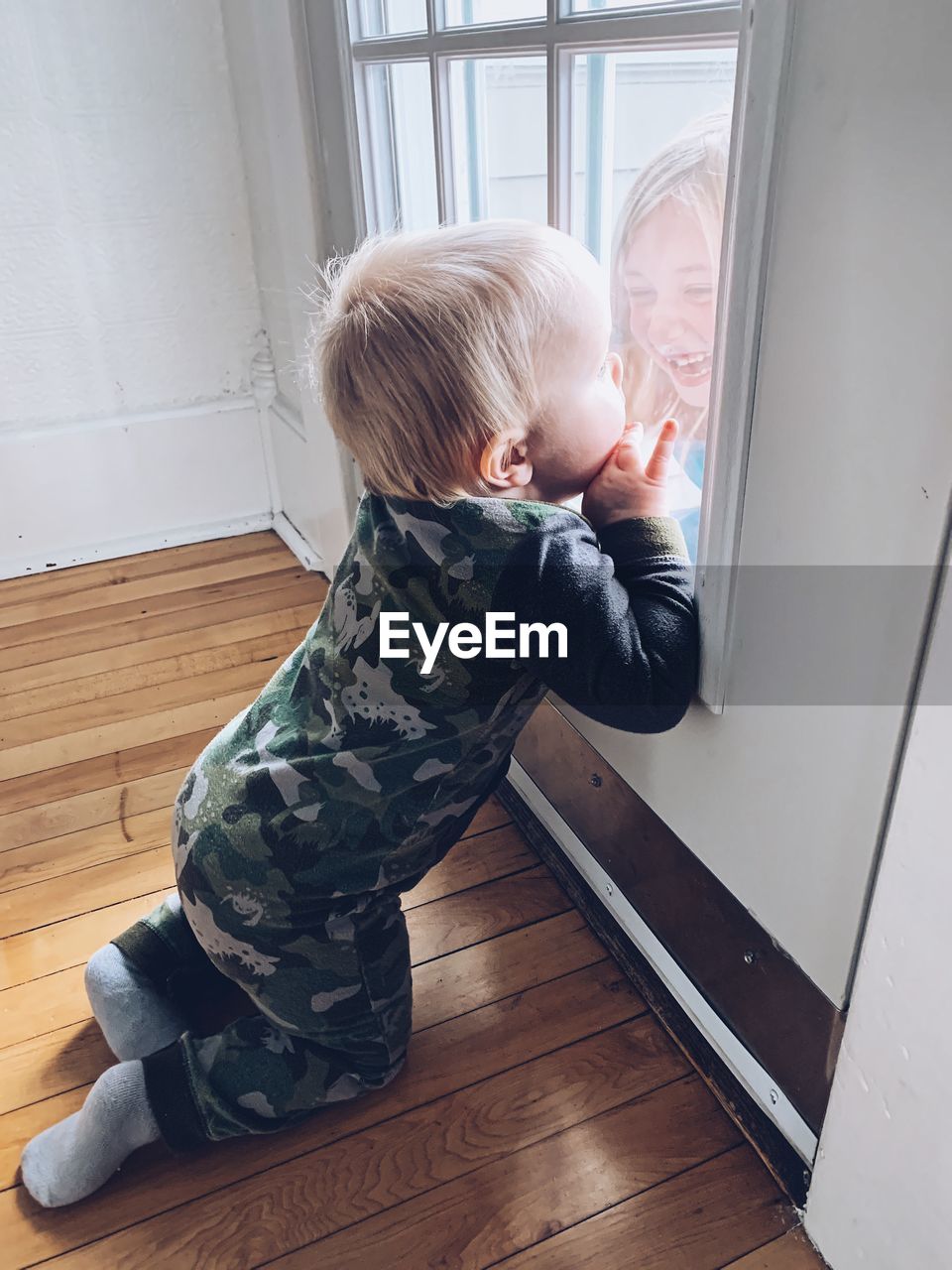 Side view of baby boy looking at sister through door at home