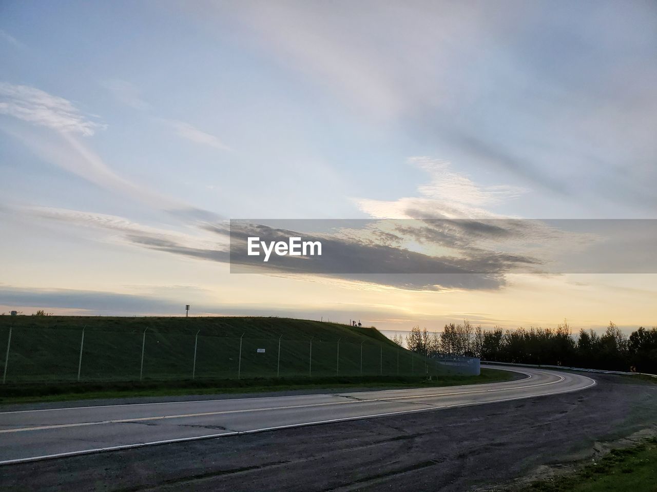 Empty road by field against sky during sunset