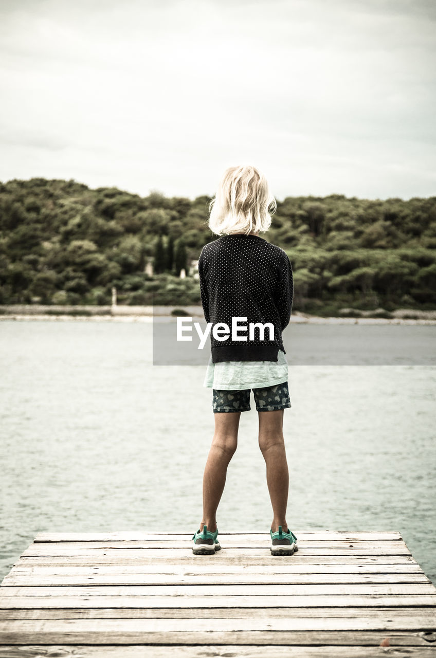 Rear view of girl standing on pier over lake against sky