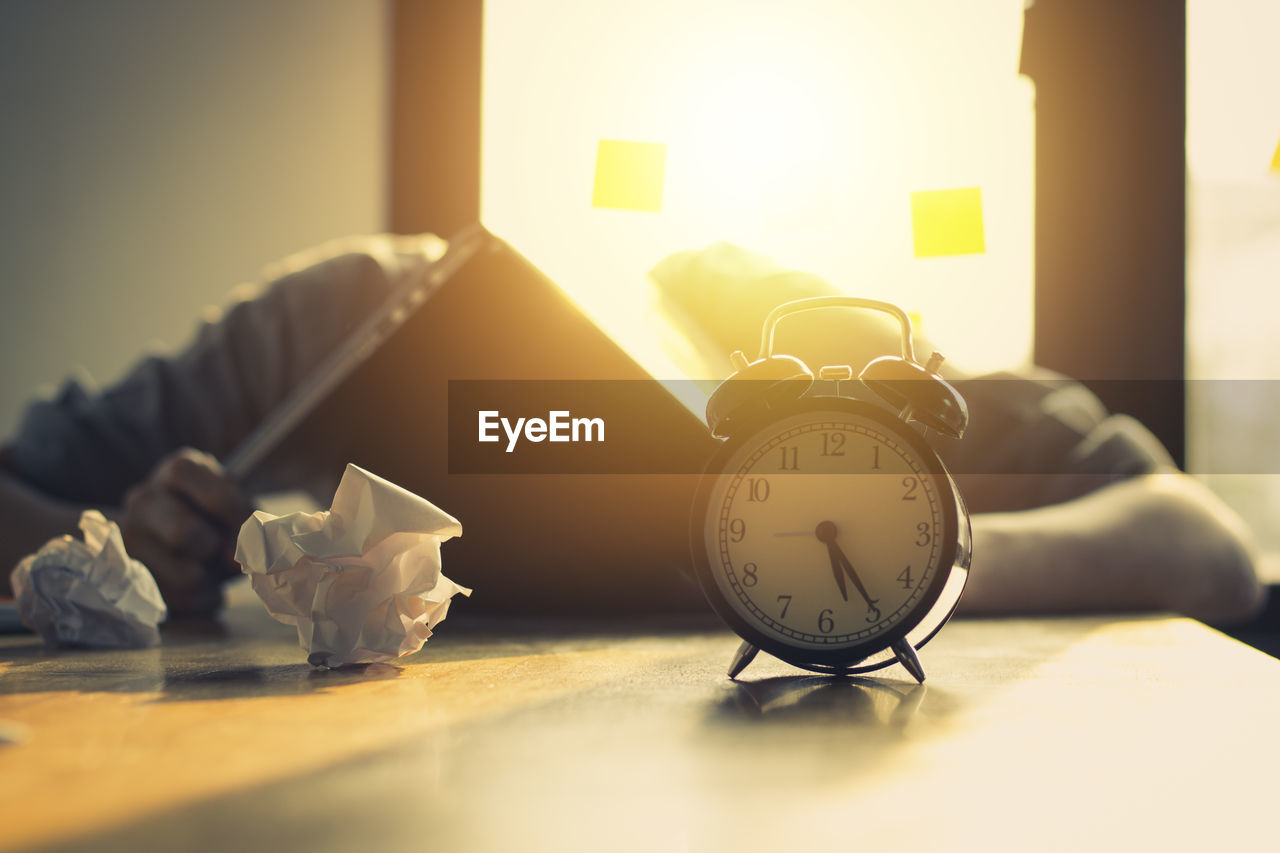 Stressed businessman with crumpled paper balls and alarm clock at desk