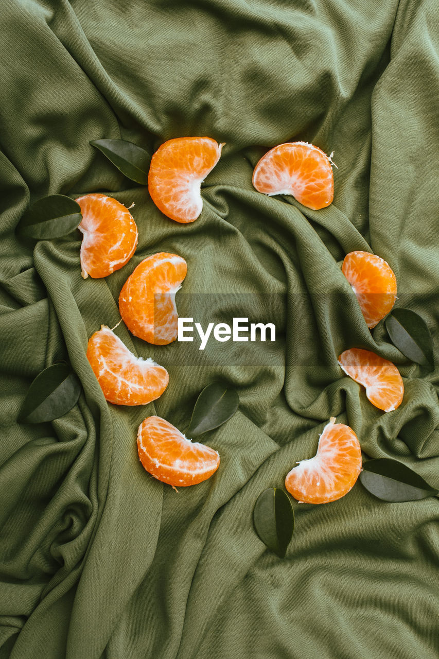 Fresh clementines with leaves on green fabric, top view