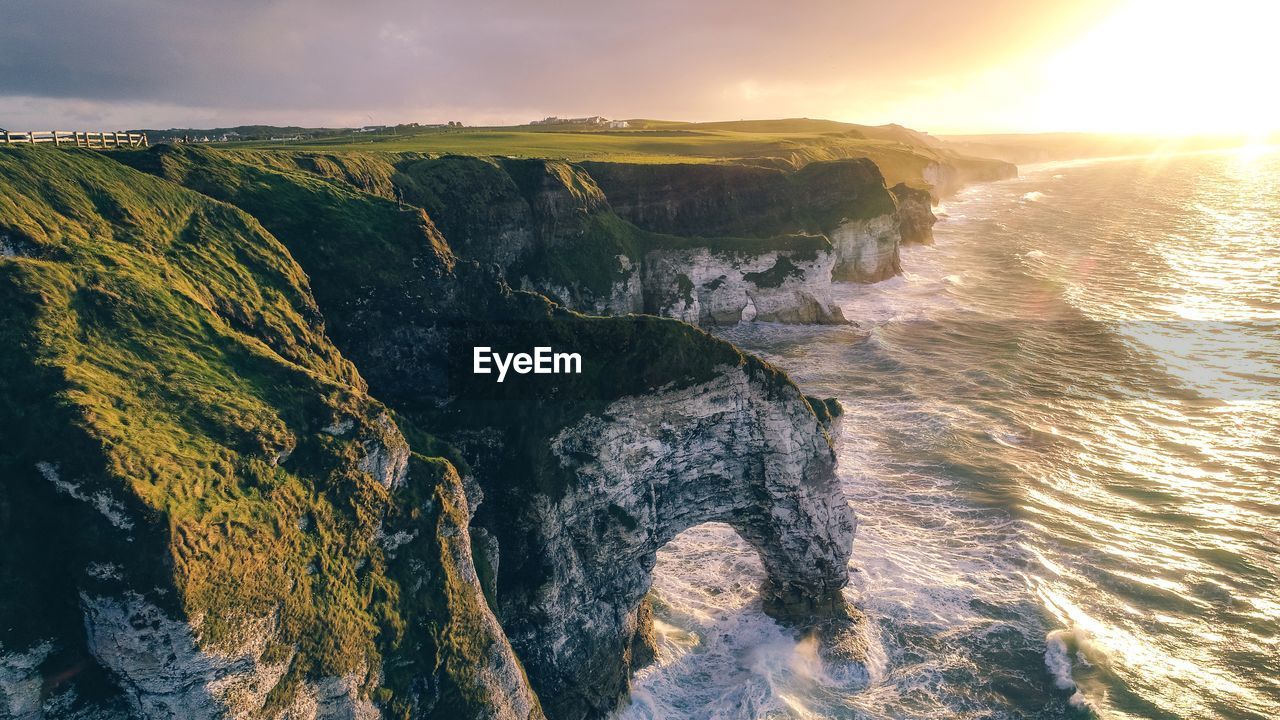 Scenic view of mountain by sea against cloudy sky during sunset