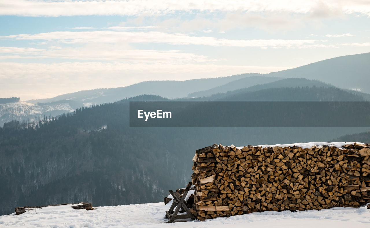 Stack of logs on snow covered mountains against sky