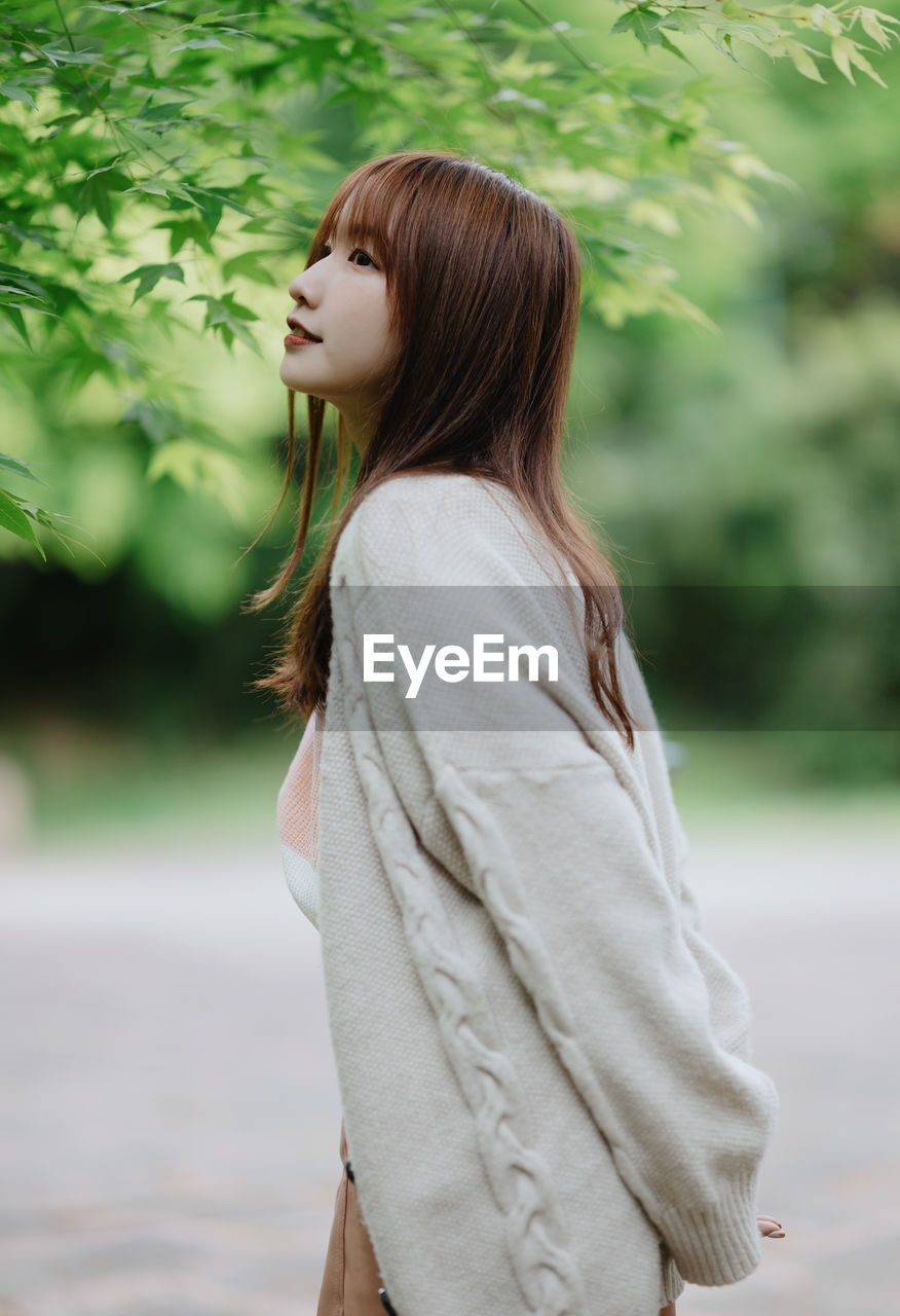 young woman looking away while standing at park