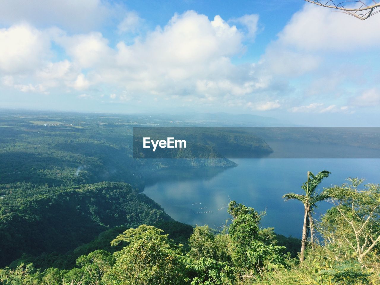 Scenic view of river and trees against cloudy sky on sunny day