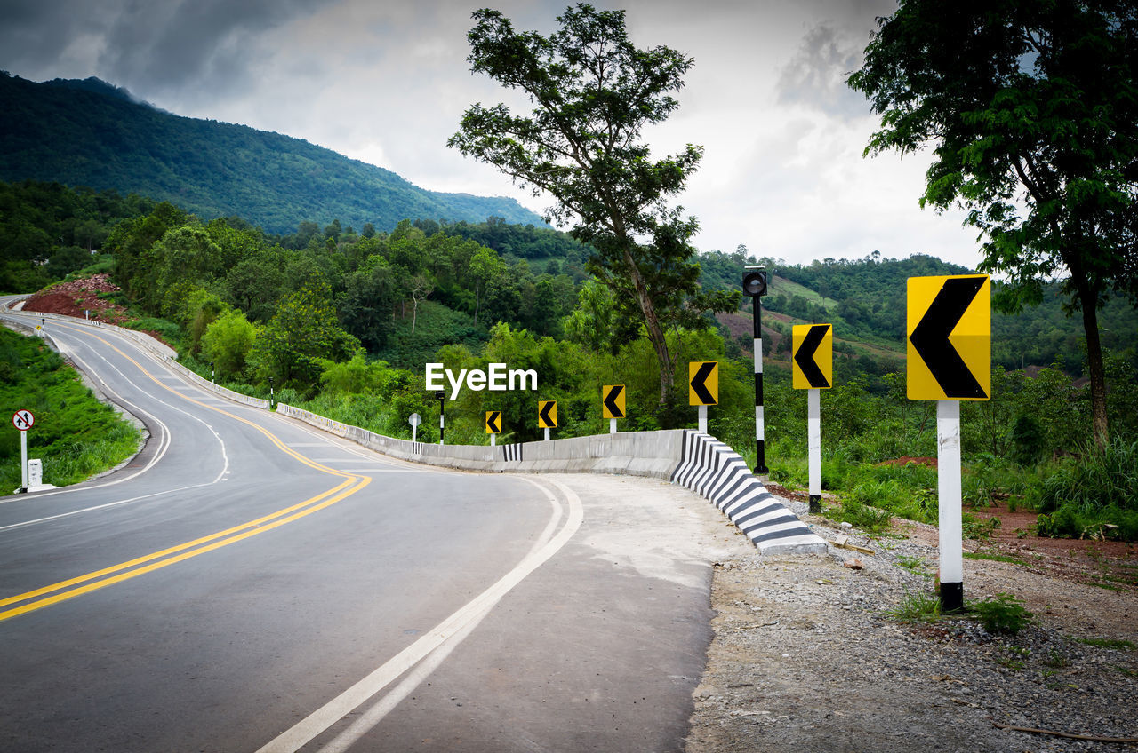 ROAD SIGN AGAINST TREES AND MOUNTAIN