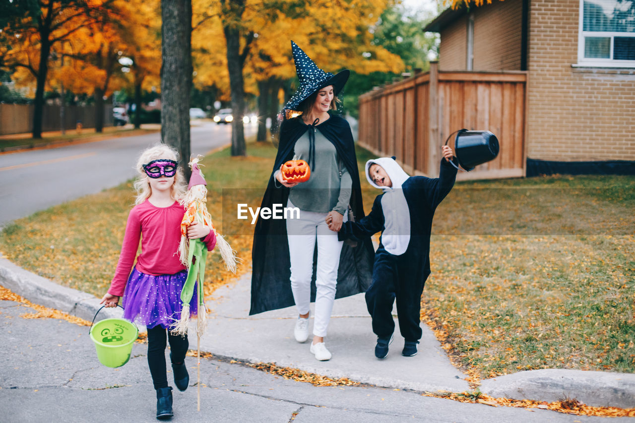 Full length portrait of mother with kids standing on tree during autumn