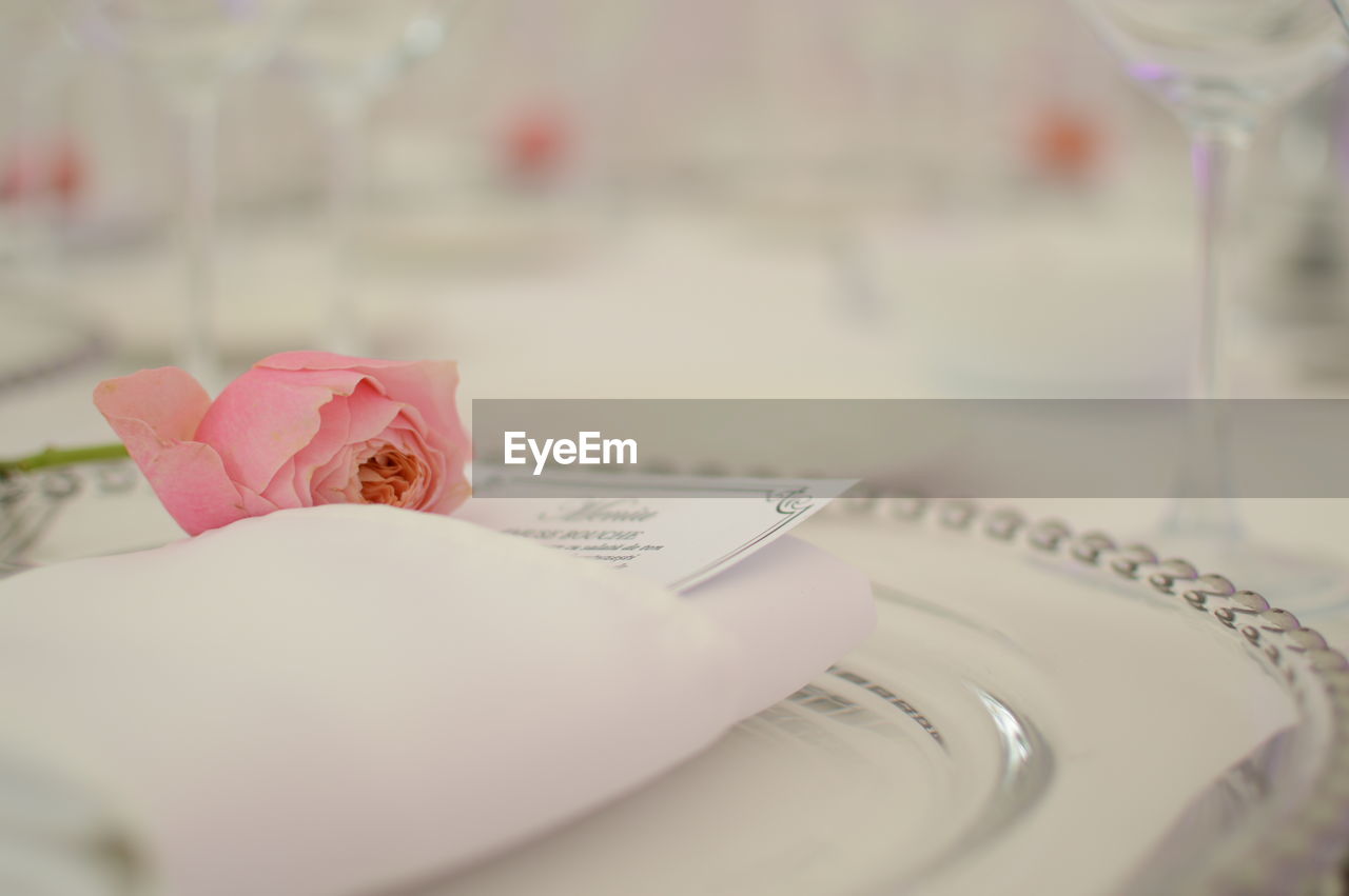 Close-up of rose with invitation card on plate at wedding reception