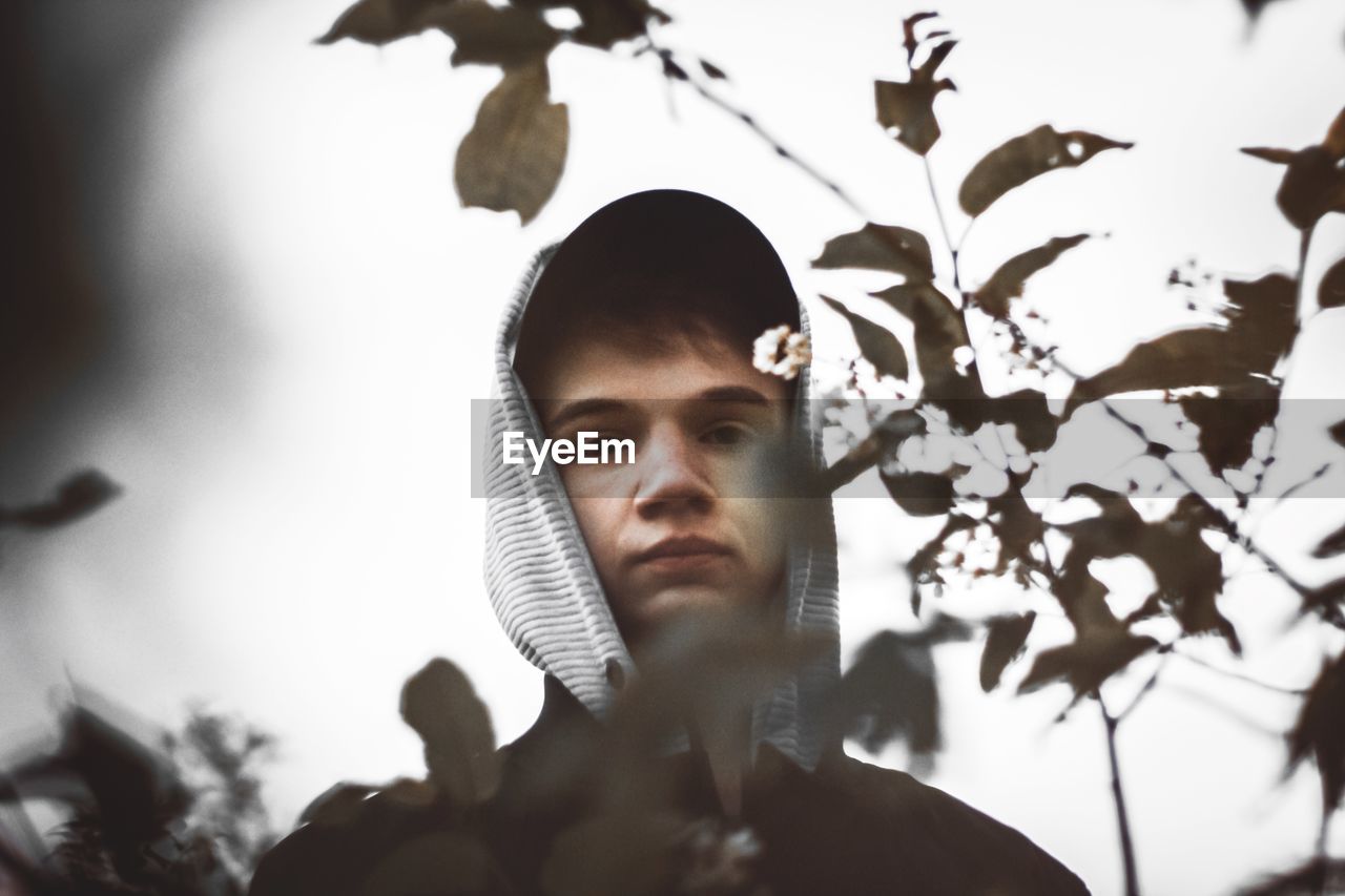 PORTRAIT OF YOUNG MAN LOOKING AWAY AGAINST PLANTS